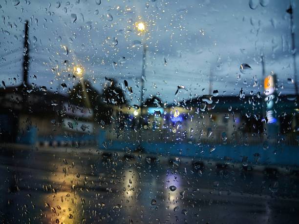 Rain droplets on a window with blurred city lights creating a moody evening scene.