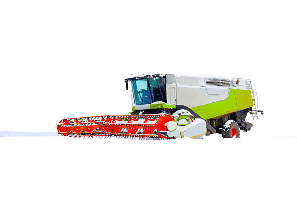 A powerful modern combine harvester with a bright red header stands in the middle of a vast white snow-covered field. The agricultural machinery is completely surrounded by snow under a bright winter sky, highlighting the scale of equipment and the end of the farming season.