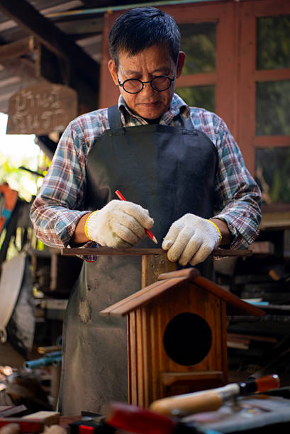 Vertical shot senior craftsman carefully works with wood showing skill experience, elderly man working carpenter craftsmanship DIY handmade projects surrounded by natural home workshop in retirement.