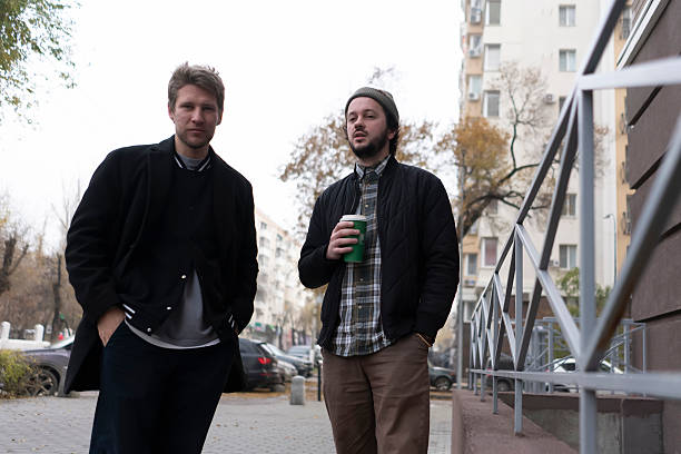 Two men stand near a building and engage in conversation while holding drinks in their hands.