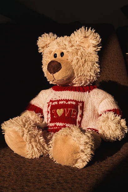 A stuffed teddy bear with a red and white striped sweater on a white background, flay lay, top view. A soft toy against the backdrop of warm summer sunshine. The bear has brown eyes and a brown nose