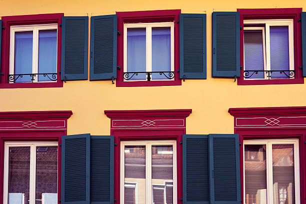 Brightly colored building features several windows with blue shutters. The architecture shows details typical of a historic area. Sunlight adds warmth to the scene.