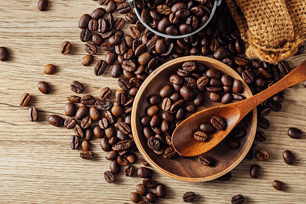 Discover a beautiful arrangement of freshly roasted coffee beans on a wooden table, complete with a spoon and a rustic basket, perfect for culinary inspiration.