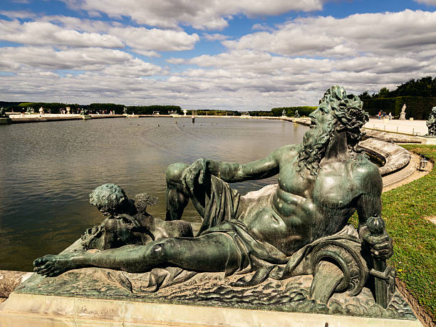 Classical river god sculpture beside a large ornamental basin in the historic gardens of the Palace of Versailles near Paris, France