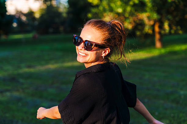 istock Cheerful woman looking over her shoulder at the camera while walking outdoors in urban park. 2255342287