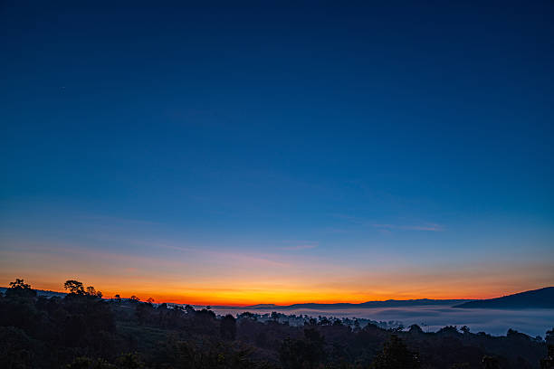 A breathtaking sunset over layered mountain ranges, with warm golden light fading into a deep blue sky, creating a serene and expansive natural landscape ideal for travel and nature themes.