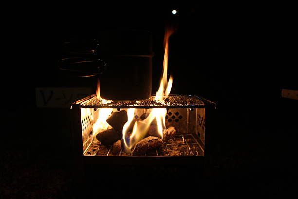 A close-up of a warm campfire at a campsite. Featuring flames and cooking utensils in the dark. Symbolic of outdoor life, relaxation, and winter camping in Japan.