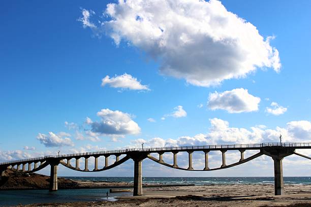 A close-up view of the unique architectural structure of Shiosai Bridge in Shizuoka, Japan. The Pacific Ocean is visible in the background under a clear winter sky. Representing Japanese civil engineering and coastal beauty.