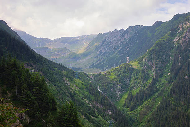 A scenic landscape view of the lush green Carpathian mountains and steep valleys along the famous Transfagarasan mountain pass in Romania under a cloudy sky.