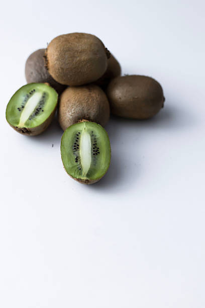 Several whole kiwis are placed in the background, while sliced kiwi halves in the foreground show bright green flesh and small black seeds.