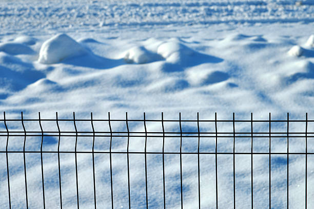 A winter scene with a view of an unpaved road behind a house fence