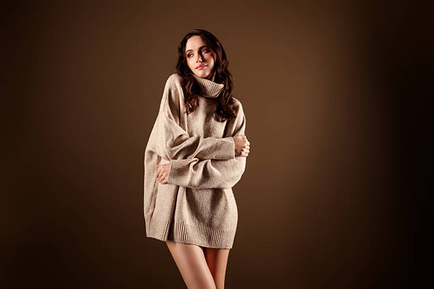 A young female model in a large beige sweater gracefully posing, showcasing modern elegance and charm against a warm gradient. Perfect for fashion concepts and lifestyle campaigns.