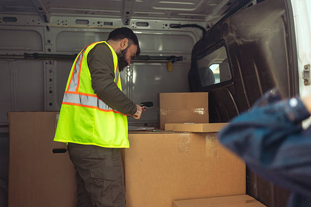 A female customer waits to collect a package from a delivery driver who scans barcodes and organizes packages inside a cargo van