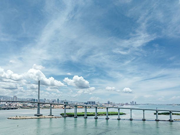 Wide view of a cable-stayed bridge spanning Cebu City's harbor, with a distant urban skyline and blue sky. Ideal stock image for travel, cityscape, and infrastructure themes in the Philippines.