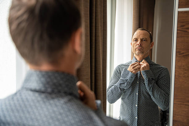istock Man buttoning his shirt while looking at himself in the mirror. Morning routine and self-care at home. 2255379790