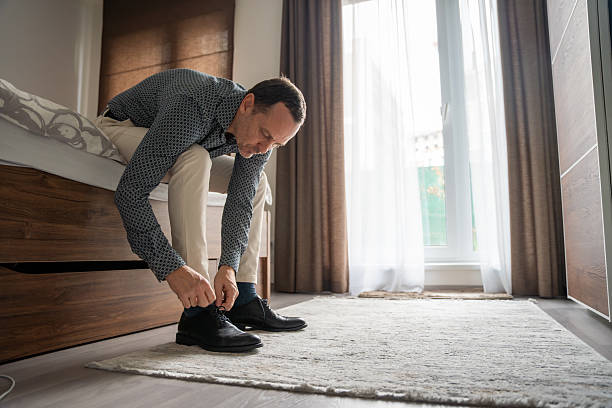 istock Man tying shoelaces while getting ready in the bedroom. Daily preparation before going out. 2255379792