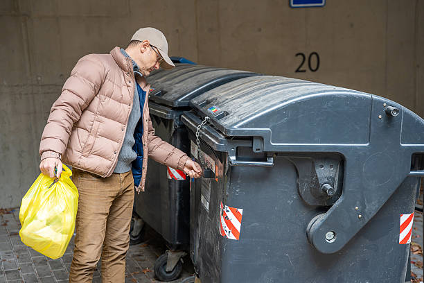 istock Man throwing garbage into a black dumpster outside. Waste management and everyday responsibilities. 2255379811