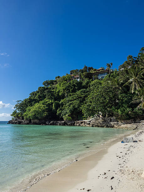 Serene tropical paradise with crystal-clear turquoise ocean waters gently lapping a pristine white sand beach. Lush jungle-covered hills rise steeply, dotted with exclusive cliffside villas, all under