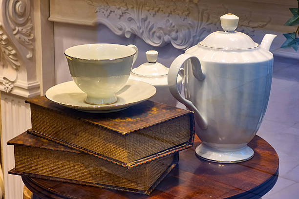 Classic still life composition featuring delicate white teapot, teacup, and saucer resting atop aged leather-bound books.