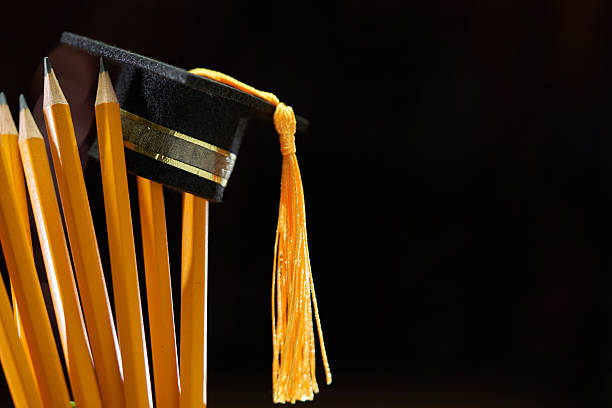 Small mortarboard graduation hat on pencil against black background