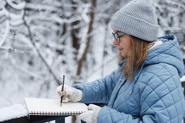 Creative woman captures winter beauty in snowy forest while sketching in her outdoor notebook
