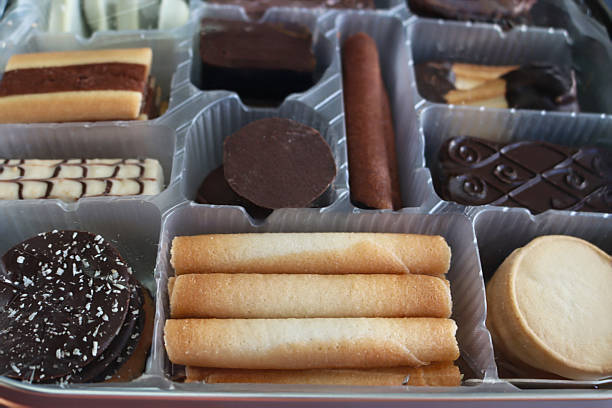Full frame image of cookie tin with disposable, single use plastic tray containing Belgian chocolate biscuit selection, crispy wafer rolls and buttery cookies coated with dark, milk or white chocolate, elevated view