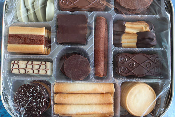 Image of cookie tin with cellophane wrapped disposable, single use plastic tray containing Belgian chocolate biscuit selection, crispy wafer rolls and buttery cookies coated with dark, milk or white chocolate, elevated view