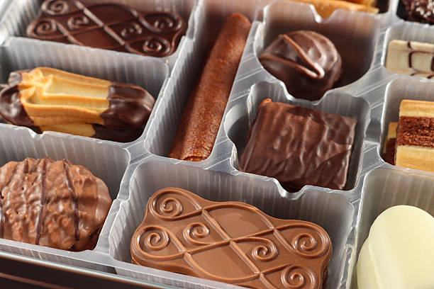 Full frame image of cookie tin with disposable, single use plastic tray containing Belgian chocolate biscuit selection, crispy wafer rolls and buttery cookies coated with dark, milk or white chocolate, elevated view, focus on foreground