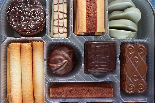 Stock photo showing close-up, elevated view of an assortment of luxury collection of Belgian chocolate biscuits in a disposable, single use plastic tray inset of a biscuit tin.