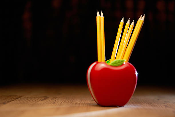 red plastic apple shape pencil holder on wood table top