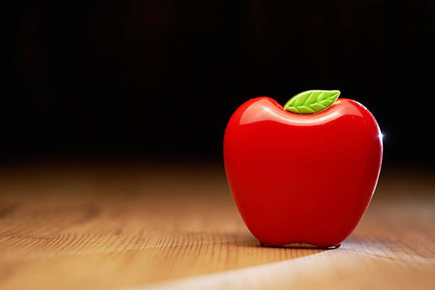 red plastic apple shape pencil holder on wood table top