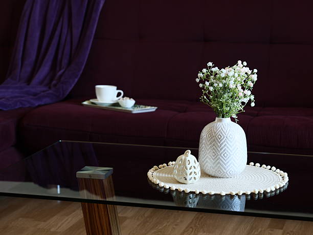 intimate sofa tea break with vase on glass table featuring gypsophila, porcelain cup and lace doily, soft maroon sofa