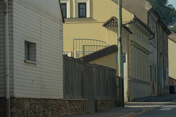 Bright facade featuring ornate balcony and fence, Sunny city courtyard with traditional window embellishments and wooden fencing