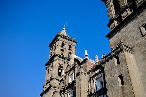 An angled view highlights Puebla cathedral’s stone tower, ornate carvings, and arched architectural details in strong daylight.