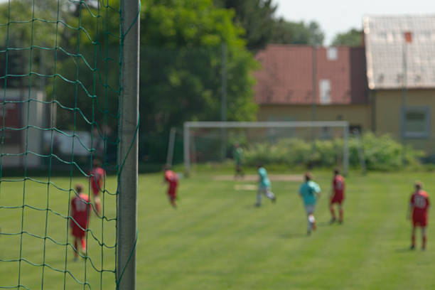 Linesman walking along sideline holding bright flag, match official moving with decisive stride while spectators and play continue