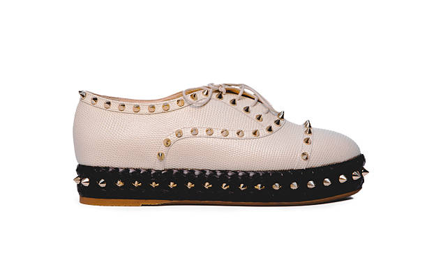 One pair of modern fashionable white sneakers rests on three natural gray stones on a lilac-pink background, close-up side view. Fashionable shoes concept.