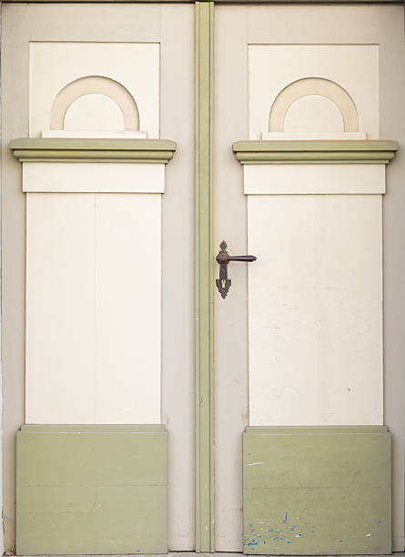Front view of pale double doors with soft semicircle motifs above tall panels in a gentle cream and green palette. An aged metal handle and subtle marks of use give the entrance a calm nostalgic feel.