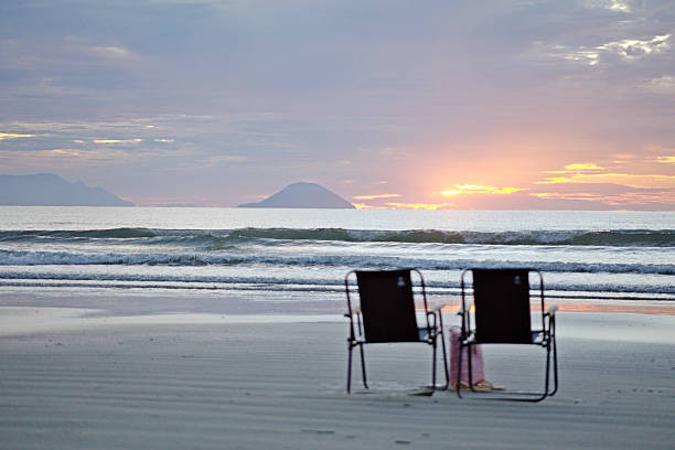 Empty chairs on the beach sand waiting for tourists. Dawn with a reddish sky, reflections of light on the sea and beach sand.
