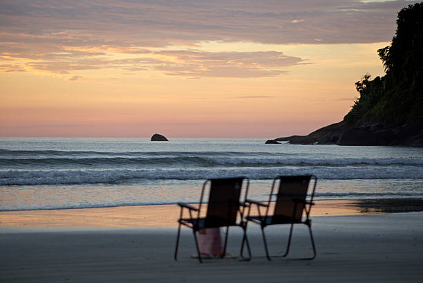 Empty chairs on the beach sand waiting for tourists. Dawn with a reddish sky, reflections of light on the sea and beach sand.