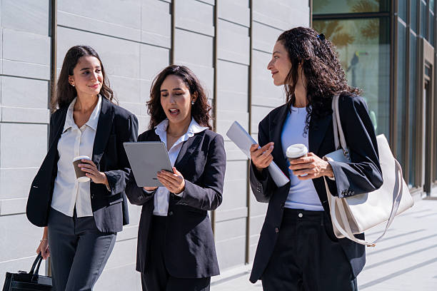 istock Three businesswomen talking and drinking coffee outdoors, showcasing teamwork, communication, and professional collaboration in a modern corporate environment. Ideal for business, leadership, and workplace concepts. 2255397359