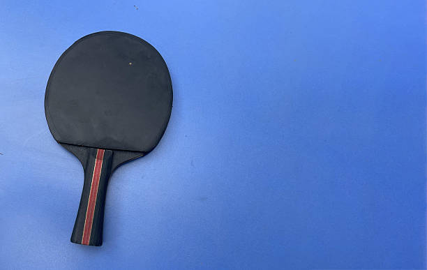 3D render of a metallic gold ping pong paddle with a matching ball on a dark, black studio surface with warm reflections—luxury sports aesthetic.