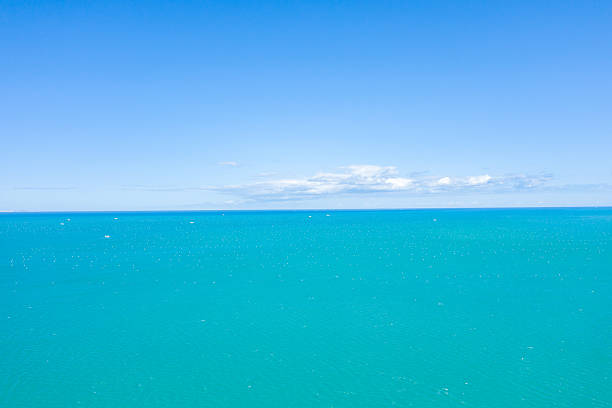 Wide open view of vivid turquoise water stretching to the distant horizon beneath a bright, cloud-dotted blue sky, creating a sense of calm and limitless space.