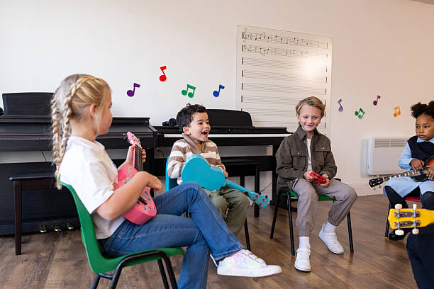 A group of happy students sitting in a circle in a bright classroom, playing colourful ukuleles and percussion instruments during a music lesson. The scene represents early childhood education, creativity, teamwork, and musical development in a preschool setting.Video for this scenario is available