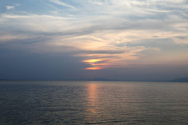 Dramatic Sunset Over Calm Sea With Soft Cloud Layers And Warm Orange Light Reflecting On Water Surface, Creating Peaceful And Atmospheric Evening Landscape With Sense Of Serenity, Nature, And Tranquil Horizon.