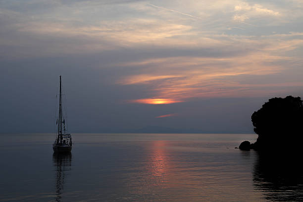 Quiet Sunset Over Calm Sea With Sailboat Silhouette And Distant Coastline, Soft Evening Light Reflecting On Water Surface, Creating Peaceful Atmosphere Of Solitude, Travel, And Tranquil Maritime Landscape.