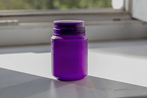 The container is filled with vibrant violet substance and illuminated by natural daylight creating interesting shadows