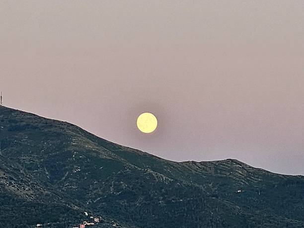 Genova, Italy - January 3, 2026: An amazing photography of the full moon over the city of Genova by night with a great clear and blue sky in the background and some stars.