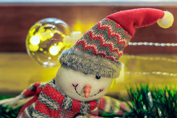 Festive holiday setup featuring a cute snowman plush and a glowing white candle on a wooden windowsill. Perfect for Christmas greeting cards and seasonal decor.