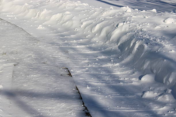 A pathway is mostly buried in snow while snowdrifts line both sides. The sun shines down on the scene. Trees can be seen in the background.