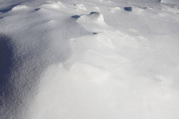 Snow blankets the ground, creating small hills and patterns under bright sunlight. The scene captures a wintry landscape with no visible trees or objects.